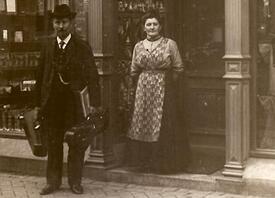 1910 Wilhelm Nagel, ausgestattet mit Instrumentenkoffern, mit seiner Ehefrau vor dem gemeinsamen Geschäft in der Deichstraße in Wilster